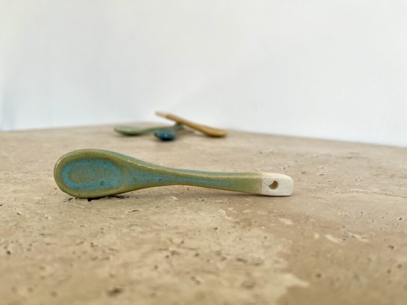 Petite cuillère vert d'eau artisanale en céramique grès blanc posée sur table